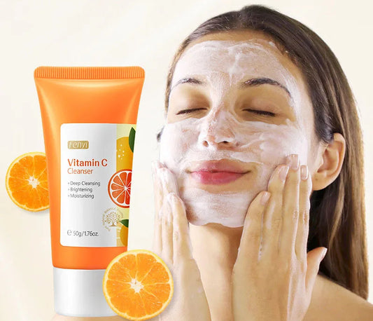 Woman applying facial cleanser with a tube of vitamin C cleanser and oranges on a light background