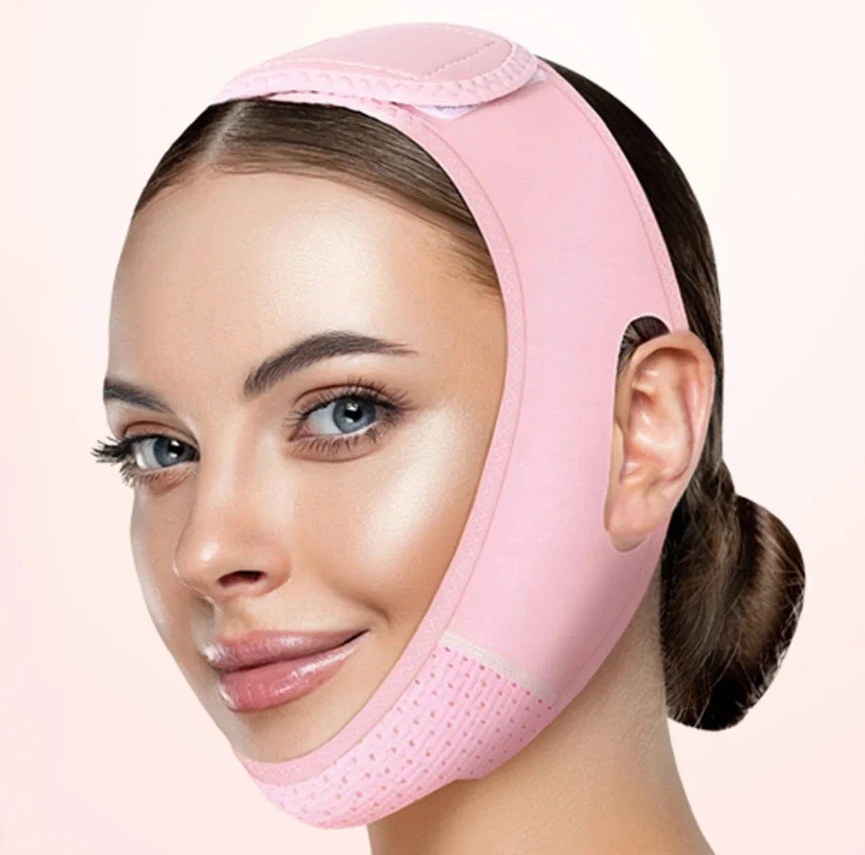 Woman wearing a pink face and neck lifting device against a light pink background